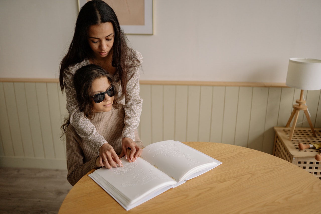 Meisje helpt een jonger meisje met het lezen van braille